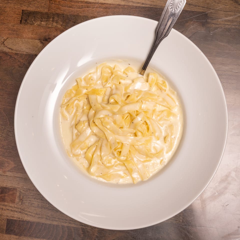 Creamy fettuccine alfredo with a fork in a white bowl on a dark wooden table.