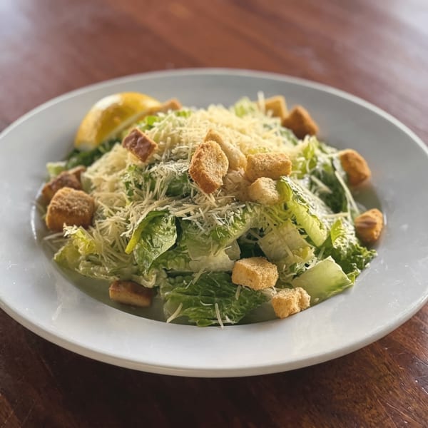 A fresh Caesar salad with romaine lettuce, croutons, parmesan cheese, and a lemon wedge on a white plate.