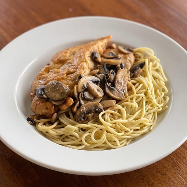 Chicken and mushrooms served over a bed of spaghetti on a white plate.