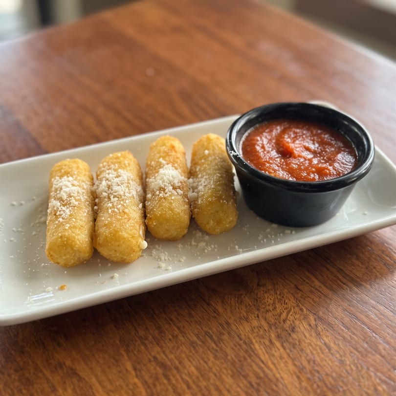 Five golden mozzarella sticks with Parmesan and a side of marinara sauce on a white plate.