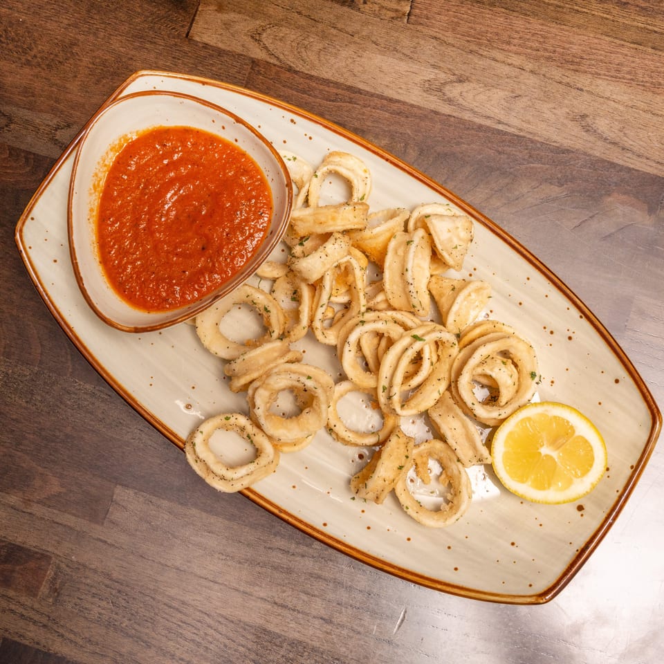Crispy fried calamari rings with a side of red marinara sauce and a lemon wedge.