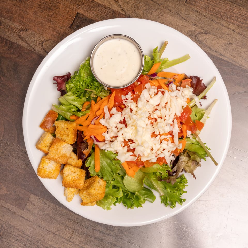 A fresh garden salad with mixed greens, shredded carrots, diced tomatoes, cheese, croutons, and ranch dressing.