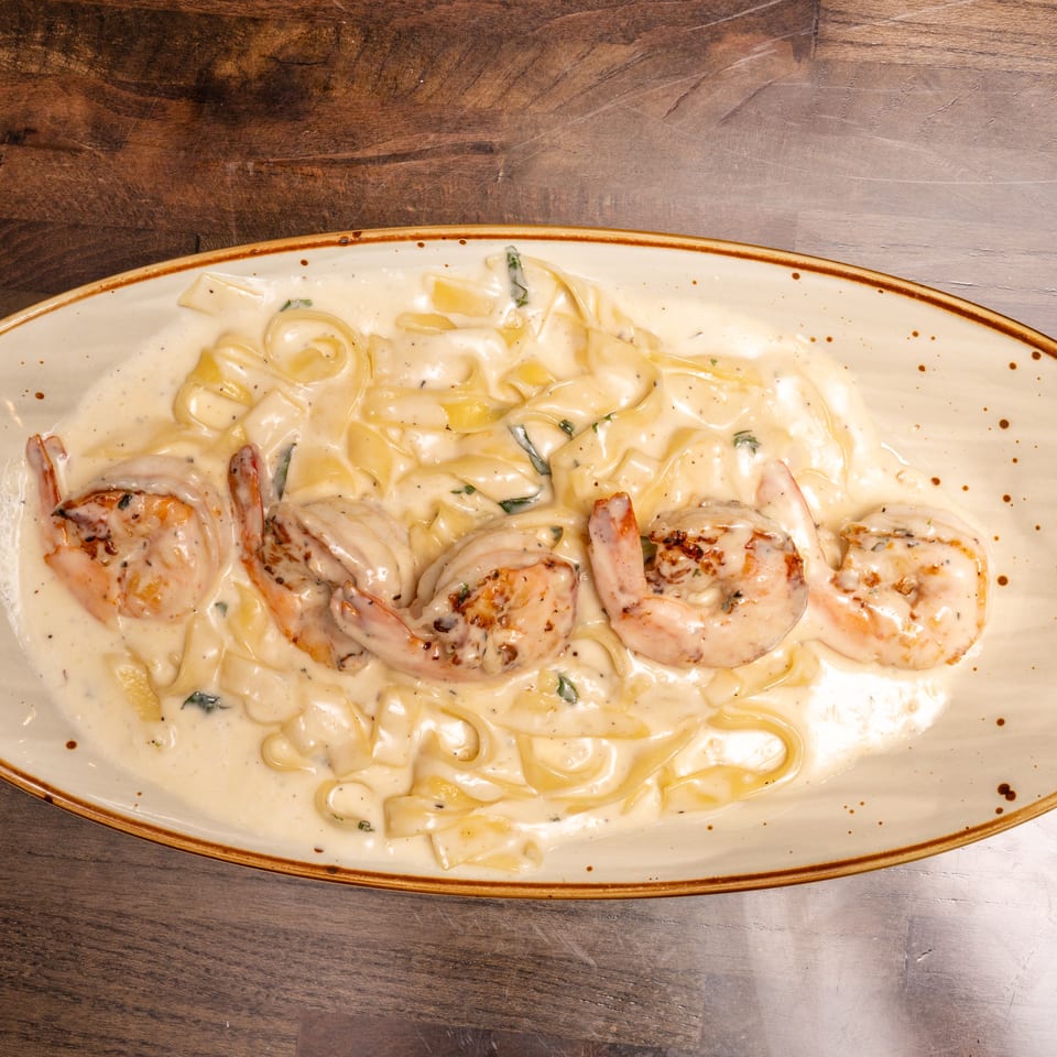Creamy fettuccine alfredo with grilled shrimp and herbs on a rectangular plate.