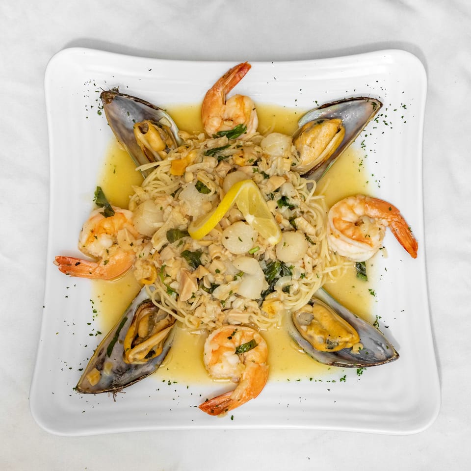 Seafood pasta with shrimp, mussels, scallops, and lemon in a white sauce on a square plate.