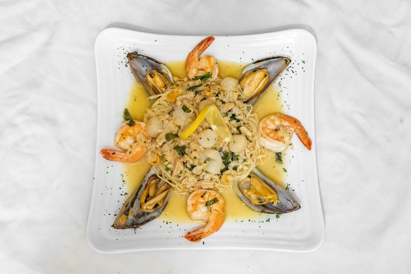 Seafood pasta with shrimp, mussels, scallops, and lemon in a white sauce on a square plate.