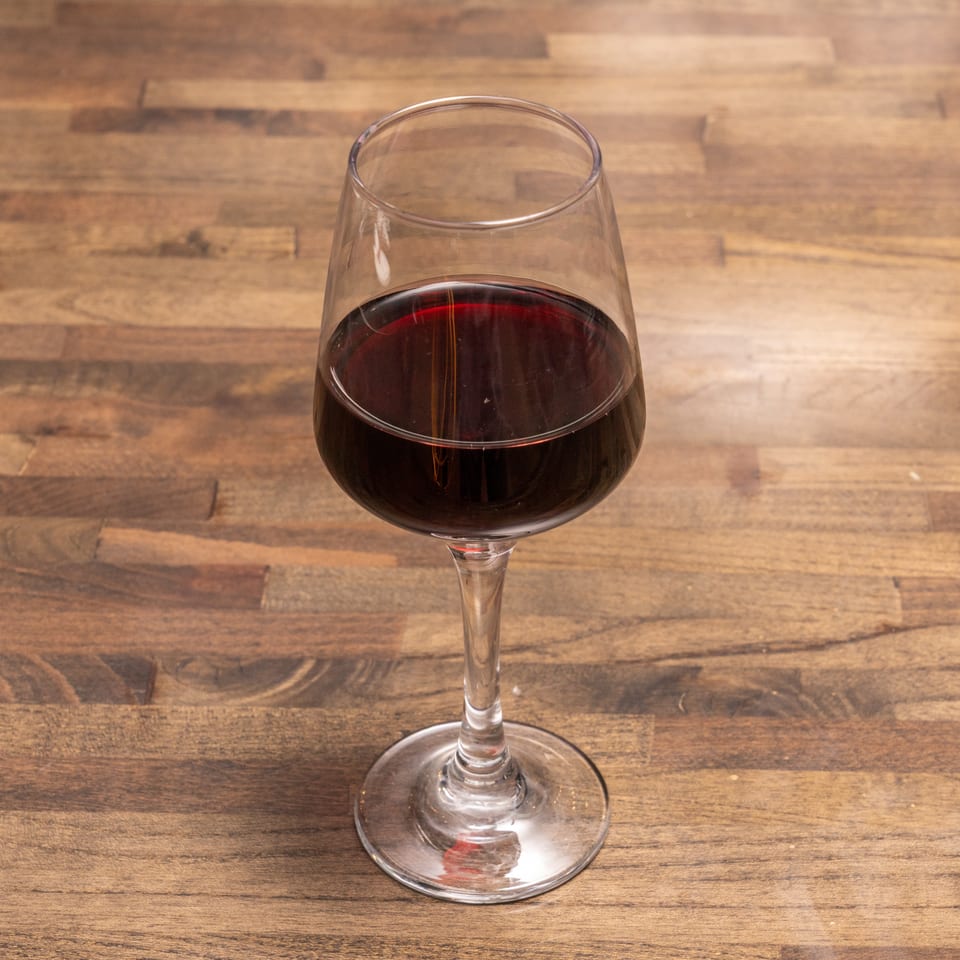 A glass of red wine sits on a rustic wooden table.