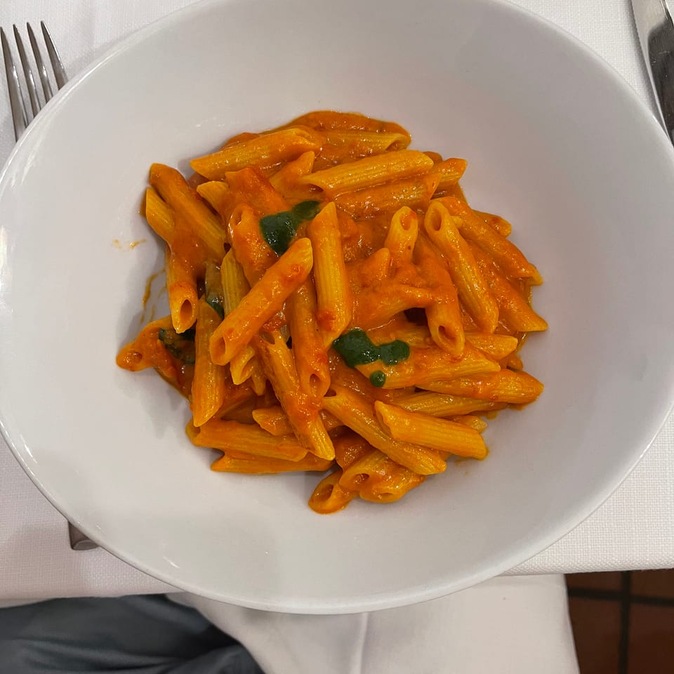 Penne pasta in a creamy orange sauce with green herbs in a white bowl on a white tablecloth.
