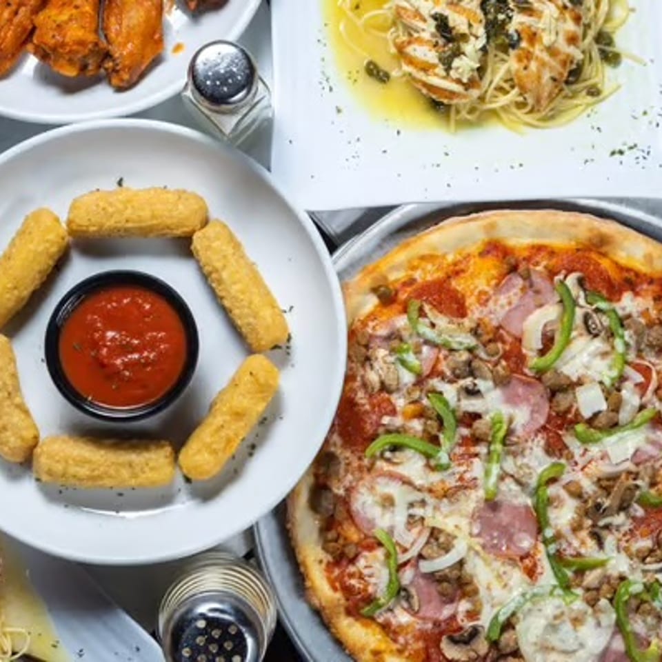 Overhead view of a table laden with various Italian dishes, including pizza, mozzarella sticks, pasta, and wings.