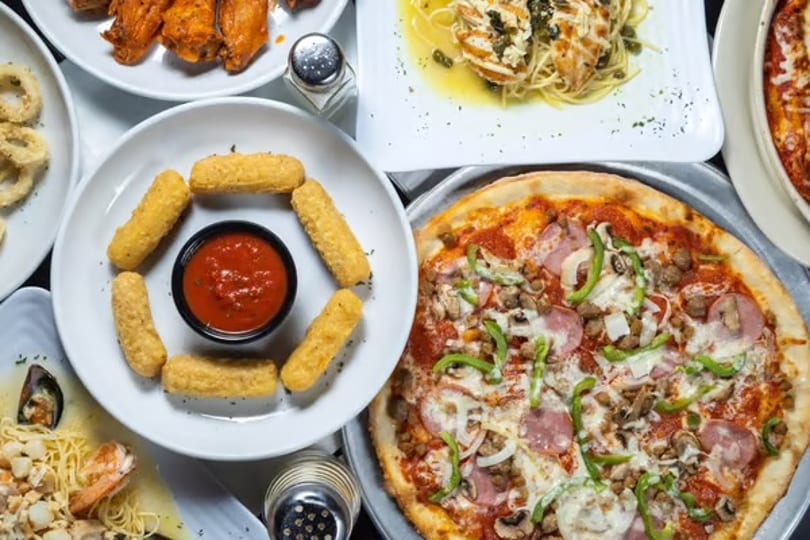 Overhead view of a table laden with various Italian dishes, including pizza, mozzarella sticks, pasta, and wings.