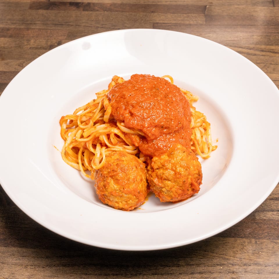 Spaghetti with a generous serving of red marinara sauce and two large meatballs on a white plate.