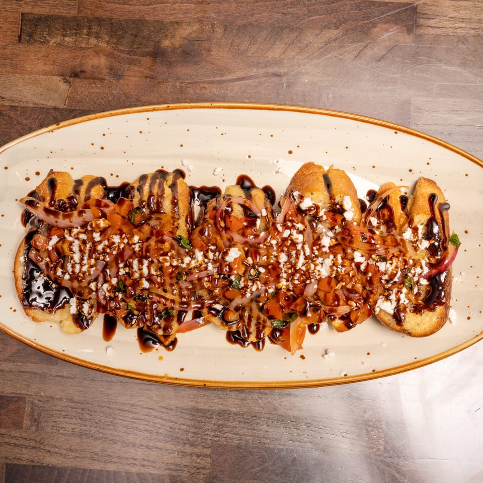 Toasted bread slices topped with diced tomatoes, onions, feta cheese, and balsamic glaze on a platter.