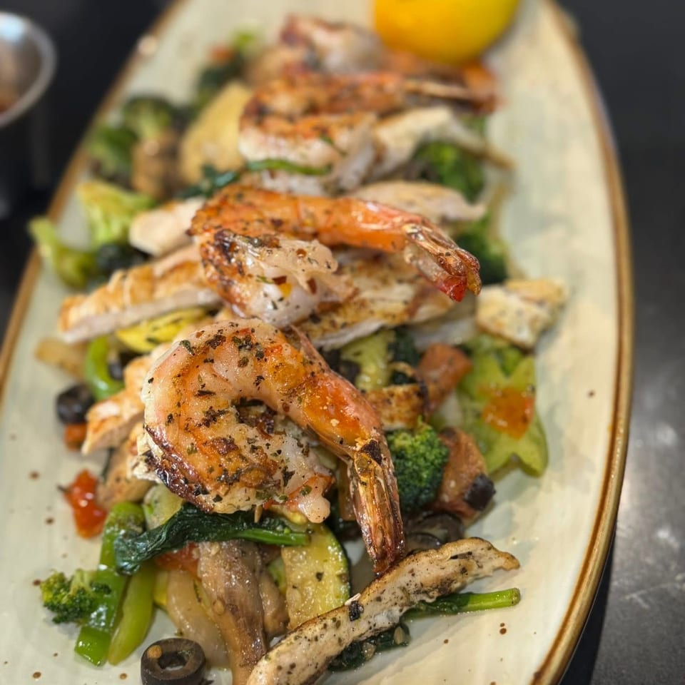 Grilled shrimp and chicken over mixed vegetables with a lemon wedge on an oblong plate.