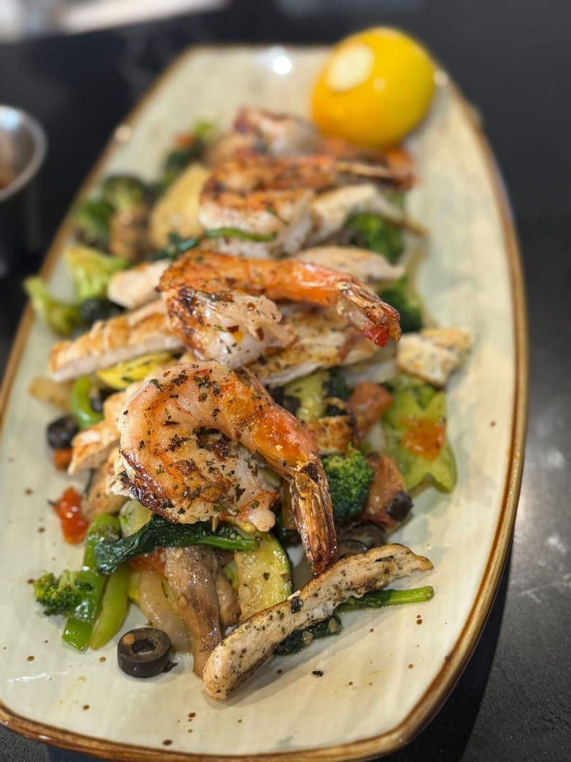 Grilled shrimp and chicken over mixed vegetables with a lemon wedge on an oblong plate.