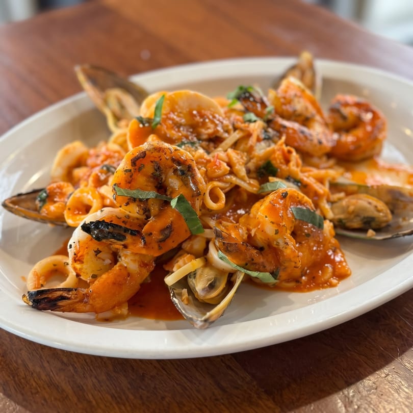 Plate of seafood pasta with grilled shrimp, mussels, calamari, and basil in a rich red sauce.