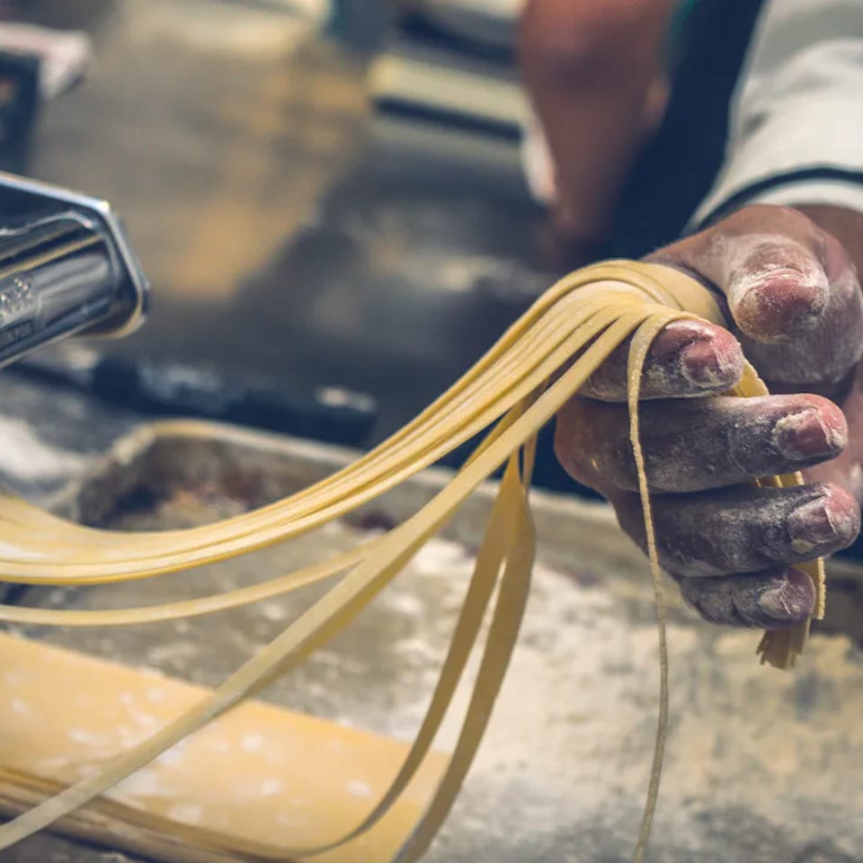 Chef's flour-dusted hands pulling fresh pasta from a pasta maker.