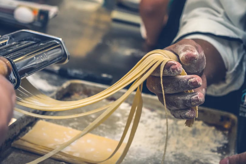 Chef's flour-dusted hands pulling fresh pasta from a pasta maker.