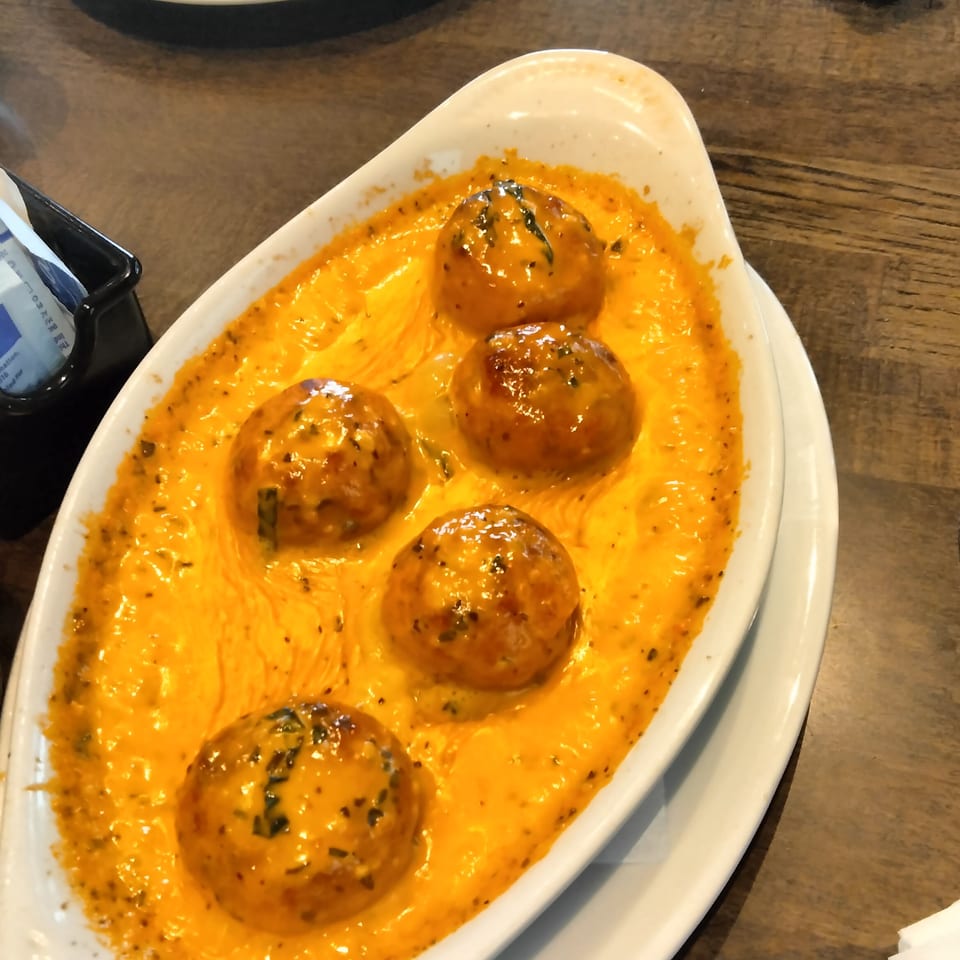 Five golden-brown meatballs in a creamy orange sauce, garnished with herbs, served in a white dish.