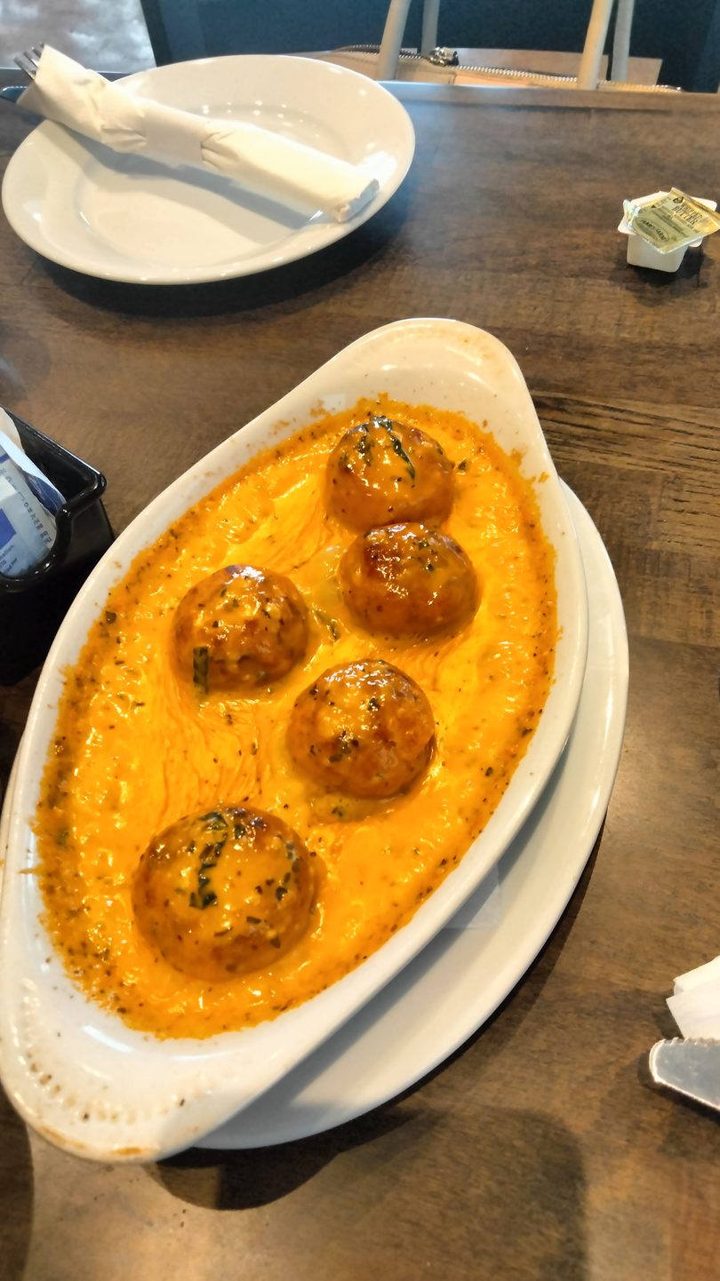 Five golden-brown meatballs in a creamy orange sauce, garnished with herbs, served in a white dish.