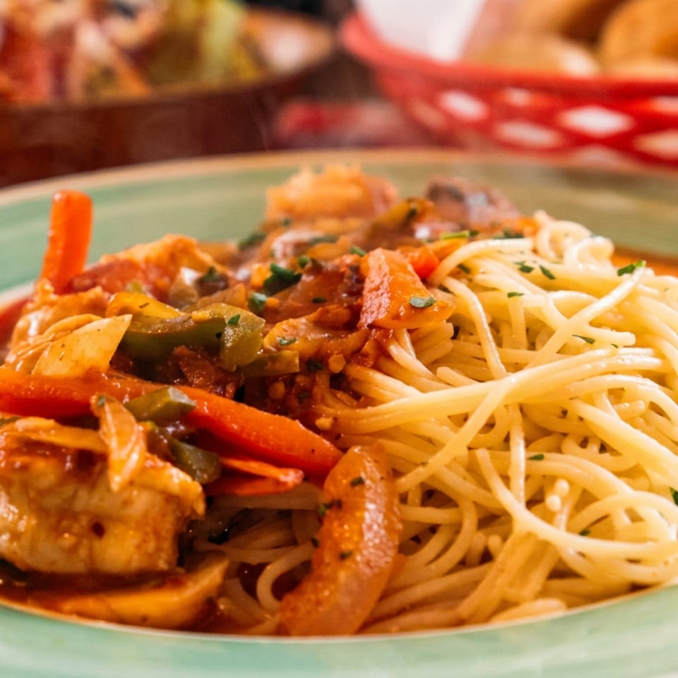 Spaghetti with shrimp, bell peppers, and mushrooms in a rich tomato sauce on a green plate.