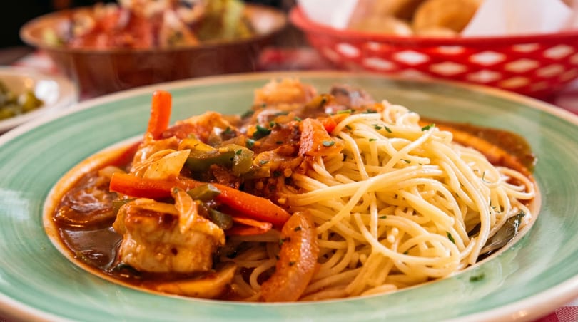 Spaghetti with shrimp, bell peppers, and mushrooms in a rich tomato sauce on a green plate.