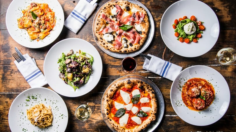 Overhead view of a rustic wooden table laden with various Italian dishes and drinks.