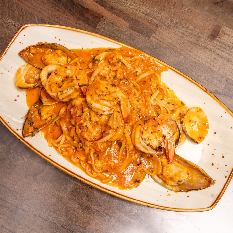 Seafood pasta with shrimp, mussels, and clams in a rich orange sauce on a white plate.