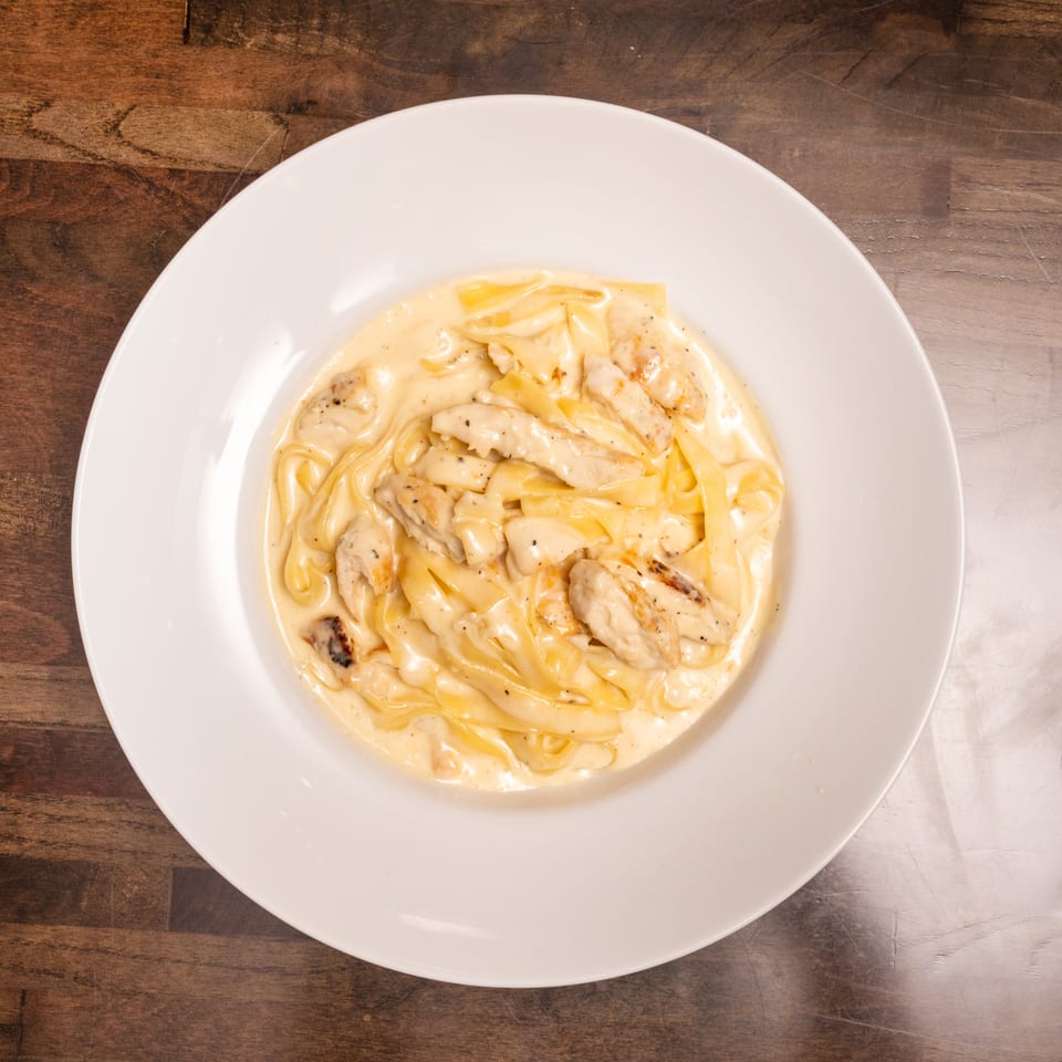 Creamy fettuccine alfredo with grilled chicken pieces served in a white bowl on a wooden table.