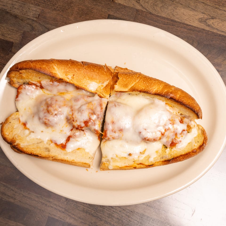Meatball sub sandwich with melted mozzarella cheese and marinara sauce on a white plate.
