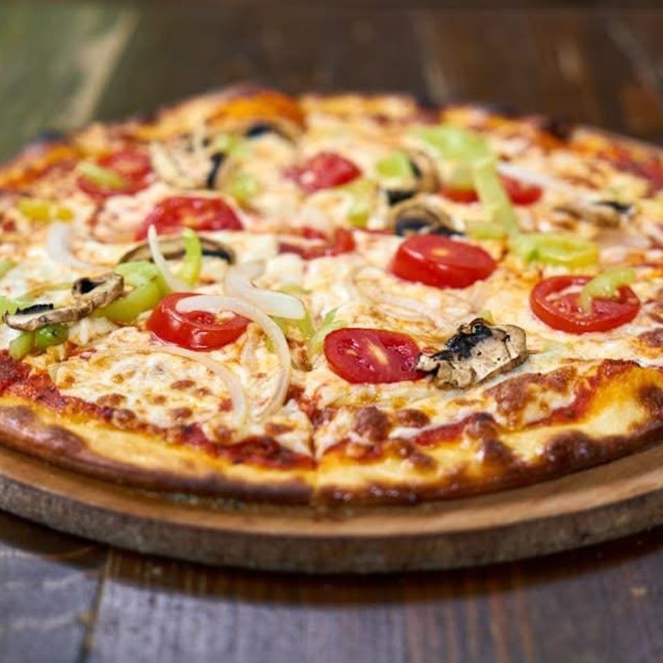 Freshly baked pizza with melted cheese, tomatoes, green peppers, onions, and mushrooms on a wooden board.