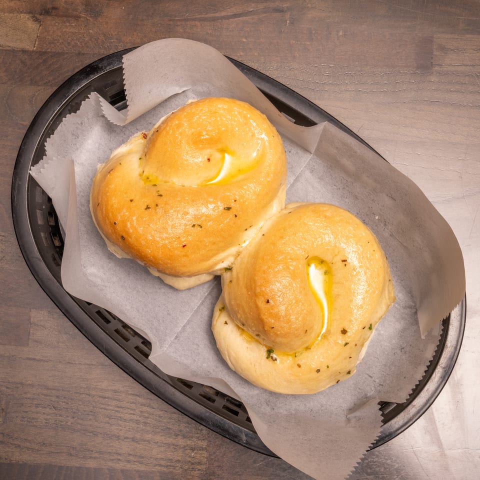 Two golden garlic knots with melted butter and herbs in a black basket on a wooden table.